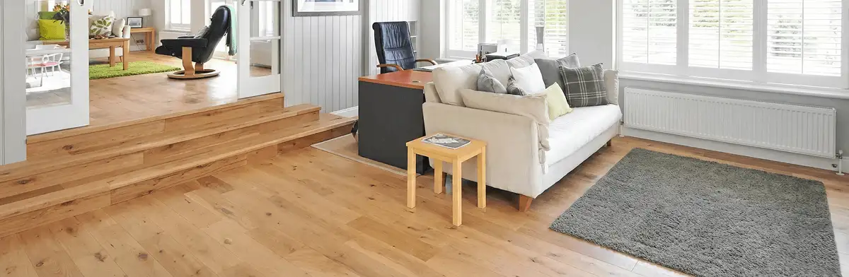 A modern living room with professionally installed laminate flooring, a beige sofa, a small side table, a gray rug, and large windows with white shutters in Cedar Rapids, IA